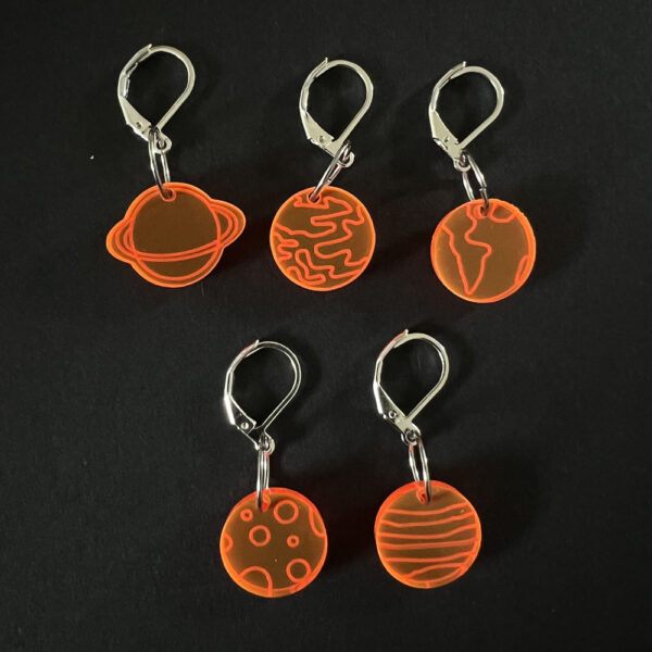 Five planets laser cut from fluorescent orange perspex, . Mounted on latch back hooks to create stitch markers.