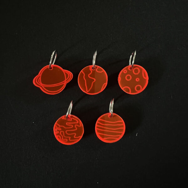 Five planets laser cut from fluorescent red perspex, . Mounted on a mix of jump rings and latch back hooks to create stitch markers.