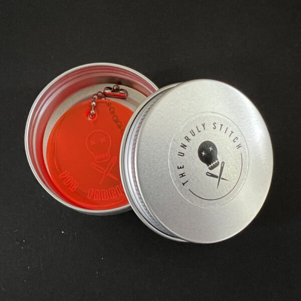 orange scissor savers in a round metal tin with The Unruly Stitch logo.
