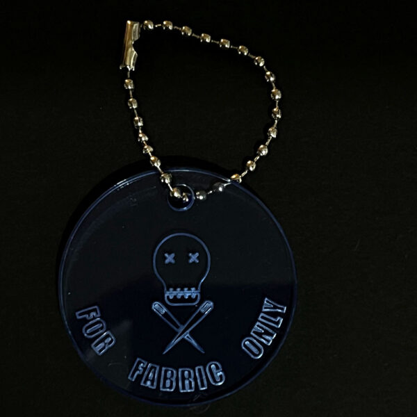 Scissor saver perspex disc on a stainless steel ball chain. The disc is cut from fluorescent blue perspex and engraved with "FOR FABRIC ONLY"and The Unruly Stitch logo