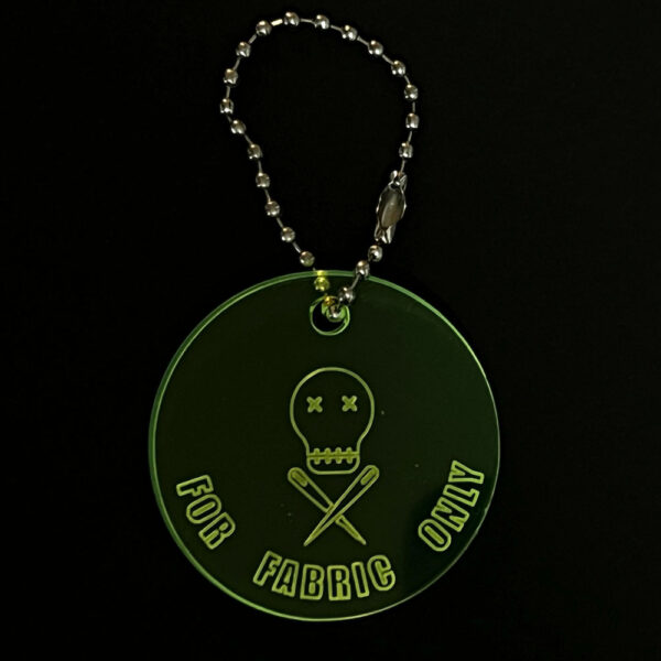 Scissor saver perspex disc on a stainless steel ball chain. The disc is cut from fluorescent green perspex and engraved with "FOR FABRIC ONLY"and The Unruly Stitch logo
