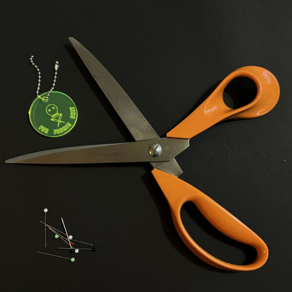 Fiskars dressmaking scissors and pins sit with a scissor saver. The connector on the ball chain is open.