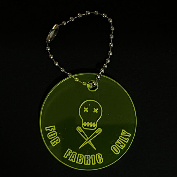 Scissor saver perspex disc on a stainless steel ball chain. The disc is cut from fluorescent yellow perspex and engraved with "FOR FABRIC ONLY"and The Unruly Stitch logo