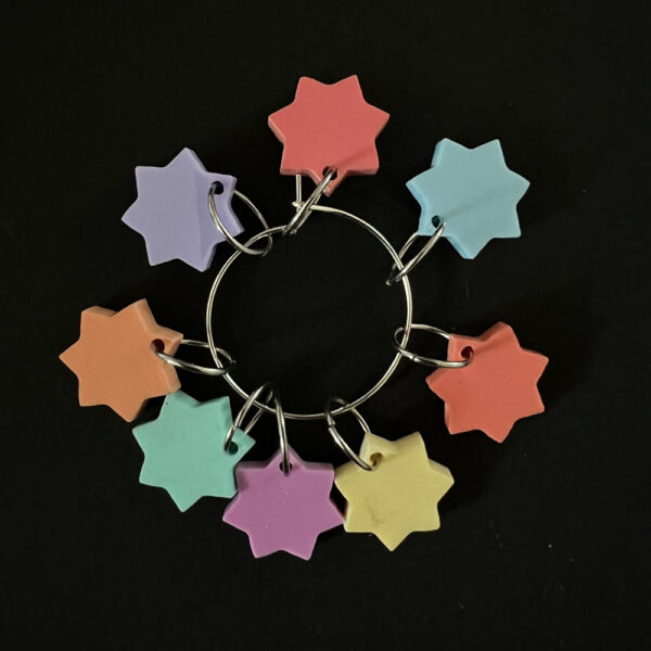 Eight stars laser cut from pastel perspex, Each star has seven points and is a different pastel colour. Mounted on a jump rings to create stitch markers.