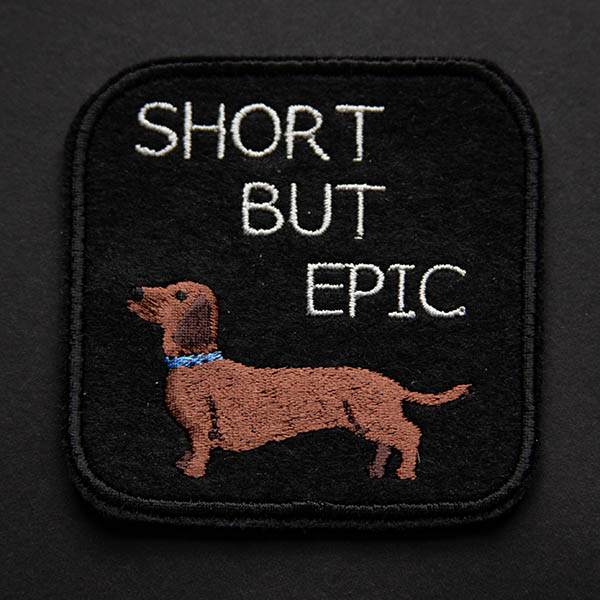 Short haired dachshund with the words short but epic embroidered patch on black felt on a black background.
