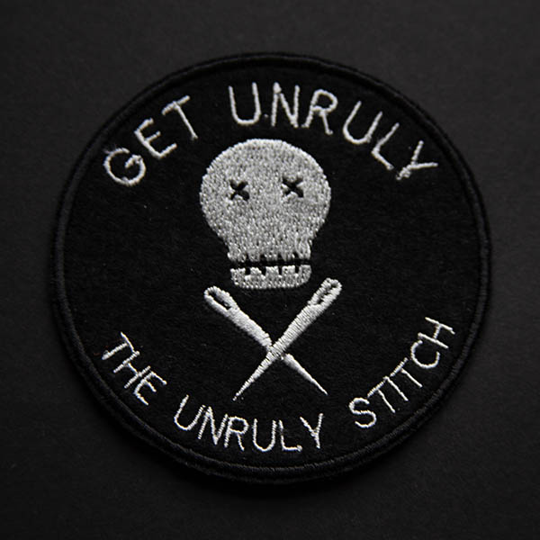 Get unruly the unruly stitch logo embroidered patch in silver on black felt on a black background.