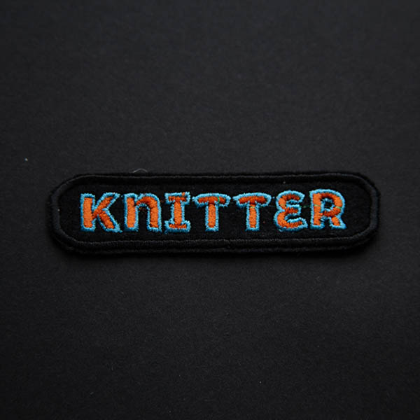 Knitter orange and turquoise embroidered patch on black felt.