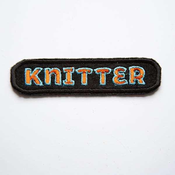 Knitter orange and turquoise embroidered patch on black felt.