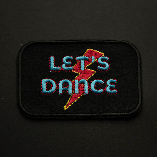 Lets dance in turquoise and red lightening bolt embroidered patch on black felt on black background.