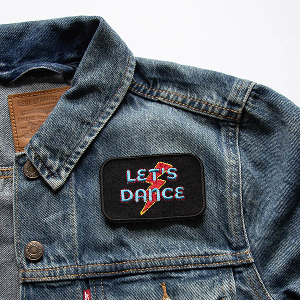 Lets dance in turquoise and red lightening bolt embroidered patch on black felt on a denim jacket.