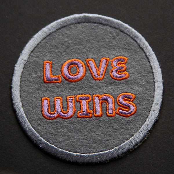 Love wins lilac and orange patch on grey felt on a black background