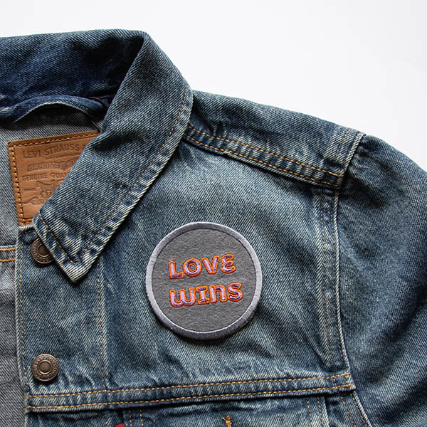 Love wins lilac and orange patch on grey felt on a denim jacket.