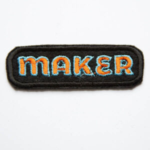 Maker embroidered patch in orange and turquoise on black felt.
