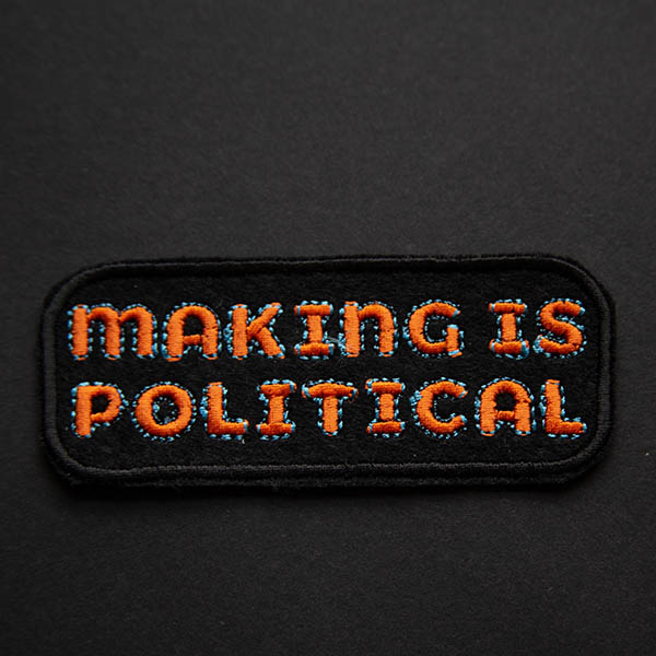 Making is political embroidered patch in orange and turquoise on black felt on a black background.