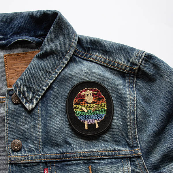 Rainbow striped sheep patch embroidered on black felt on a denim jacket.