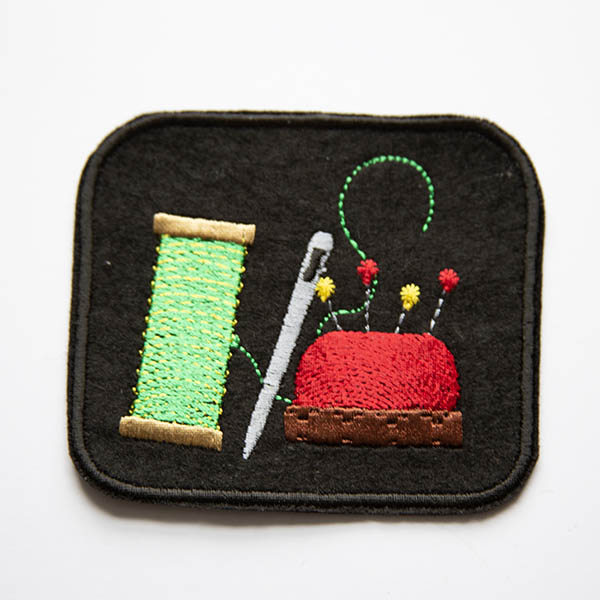 Thread needle and pin cushion embroidered on black felt patch.