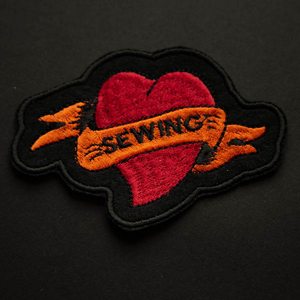 Sewing tattoo heart embroidered patch on black felt on a black background.