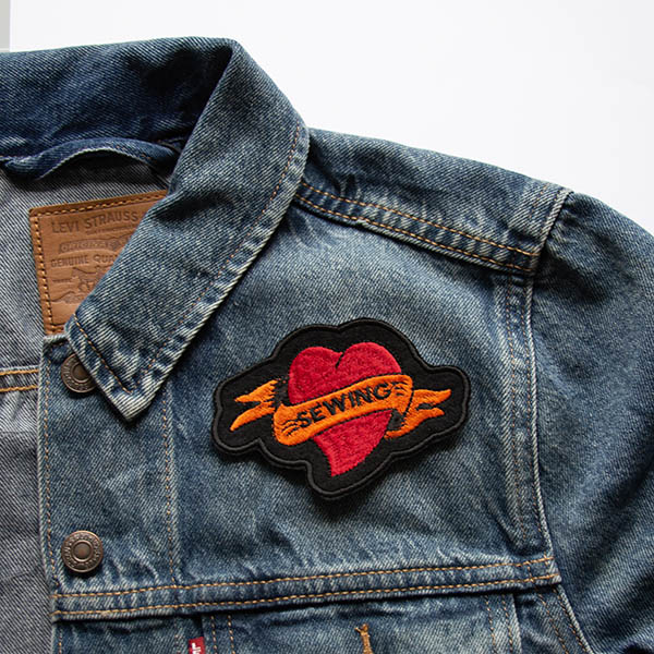 Sewing tattoo heart embroidered patch on black felt on a denim jacket.