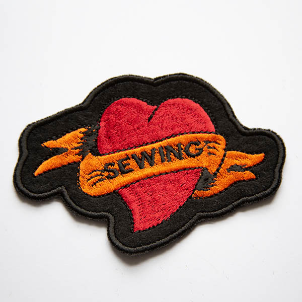 Sewing tattoo heart embroidered patch on black felt.