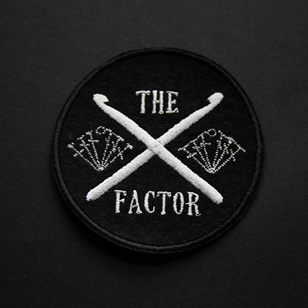 the crossed crochet hooks factor embroidered in silver on black felt on a black background.