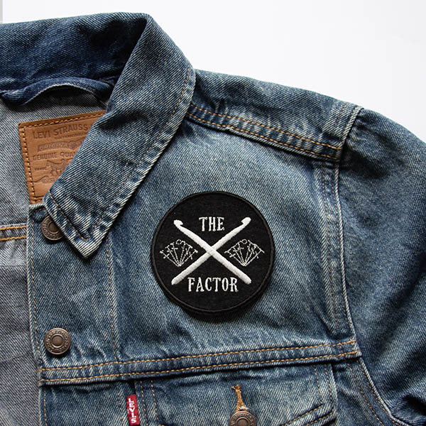 the crossed crochet hooks factor embroidered in silver on a black felt background on a denim jacket.