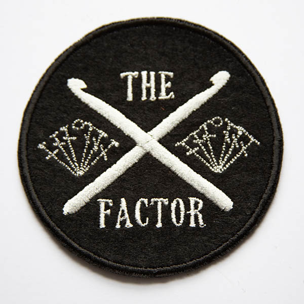 the crossed crochet hooks factor embroidered in silver on a black felt background.