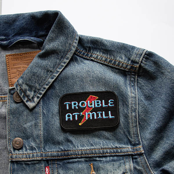 Trouble at mill overlaying lightening bolt embroidered on black felt patch on denim jacket.