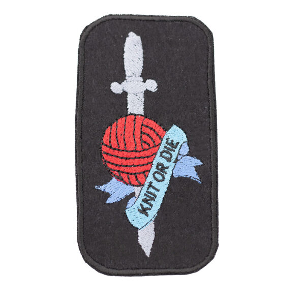 Embroidered patch on black felt showing tattoo style dagger and ball of yarn with banner. Text reads " KNIT OR DIE" . Shown on a white background.