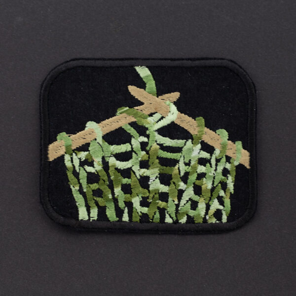 Embroidered patch showing knitting on knitting pins on black felt on black background