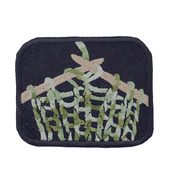 Embroidered patch showing knitting on knitting pins on black felt on white background