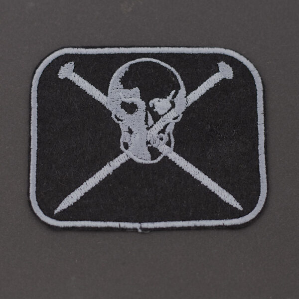 Embroidered patch showing a skull and crossed knitting pins on black felt on dark background