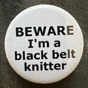 Pin badge with the words BEWARE I'm a black belt knitter. Black text, white background.