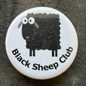 Pin badge with the words Black Sheep Club and cartoon of a black sheep. Black text, white background.