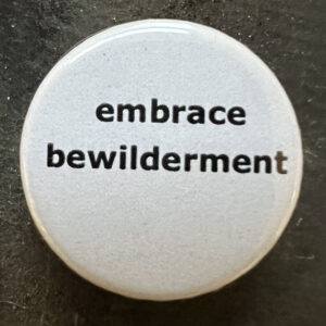 Pin badge with the words embrace bewilderment. Black text, white background.