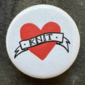 Pin badge with the tattoo style heart and banner and the word KNIT. Black text, white background.