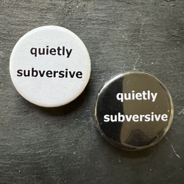Two pin badges with the words quietly subversive. Black text, white background and white text, black background.