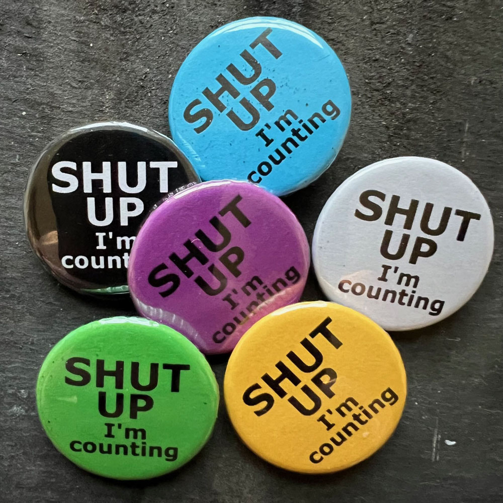 Six badges with the words SHUT UP I'm counting. Black text on blue, yellow, green, pink and white, white text on black background.