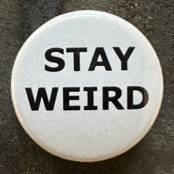 Pin badge with the words STAY WEIRD. Black text, white background.