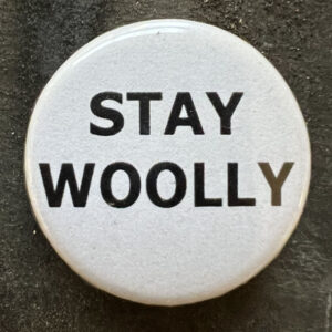 Pin badge with the words STAY WOOLY. Black text, white background.