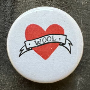 Pin badge with the tattoo style heart and banner and the word WOOL. Black text, white background.