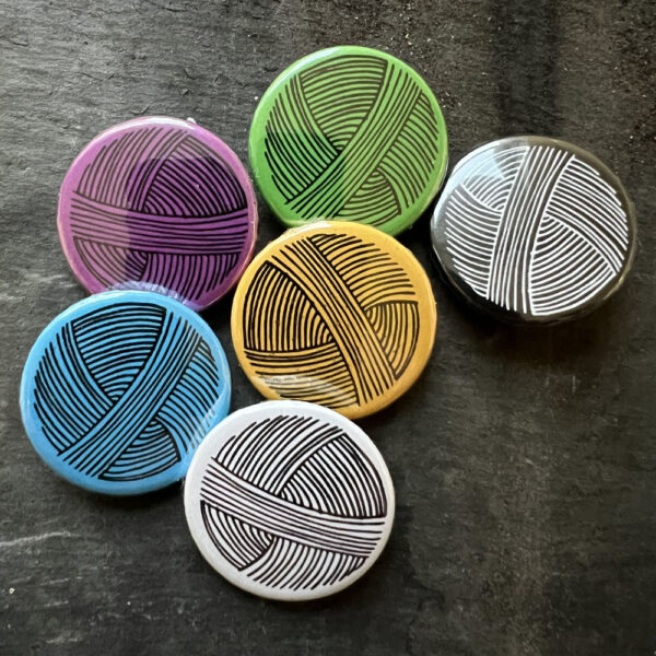 Six badges with a line drawing of a ball of yarn. Black lines on blue, yellow, green, pink and white, white lines on black background.